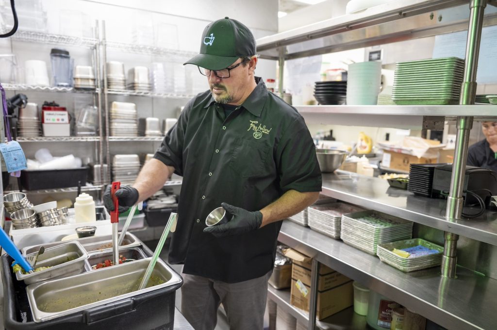 A chef in a kitchen scoops out pico de gallo.