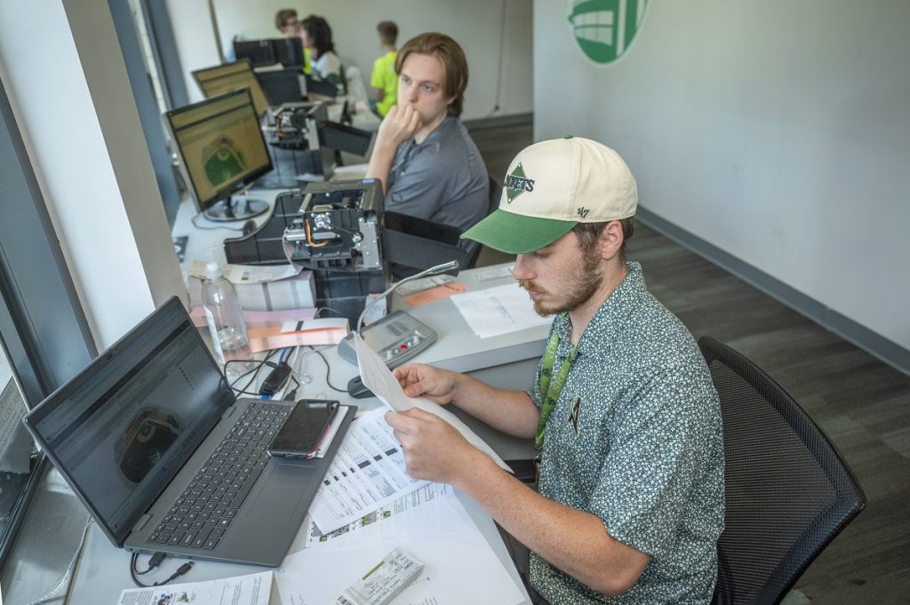 Two young men work in a ticket box office of a local baseball team.