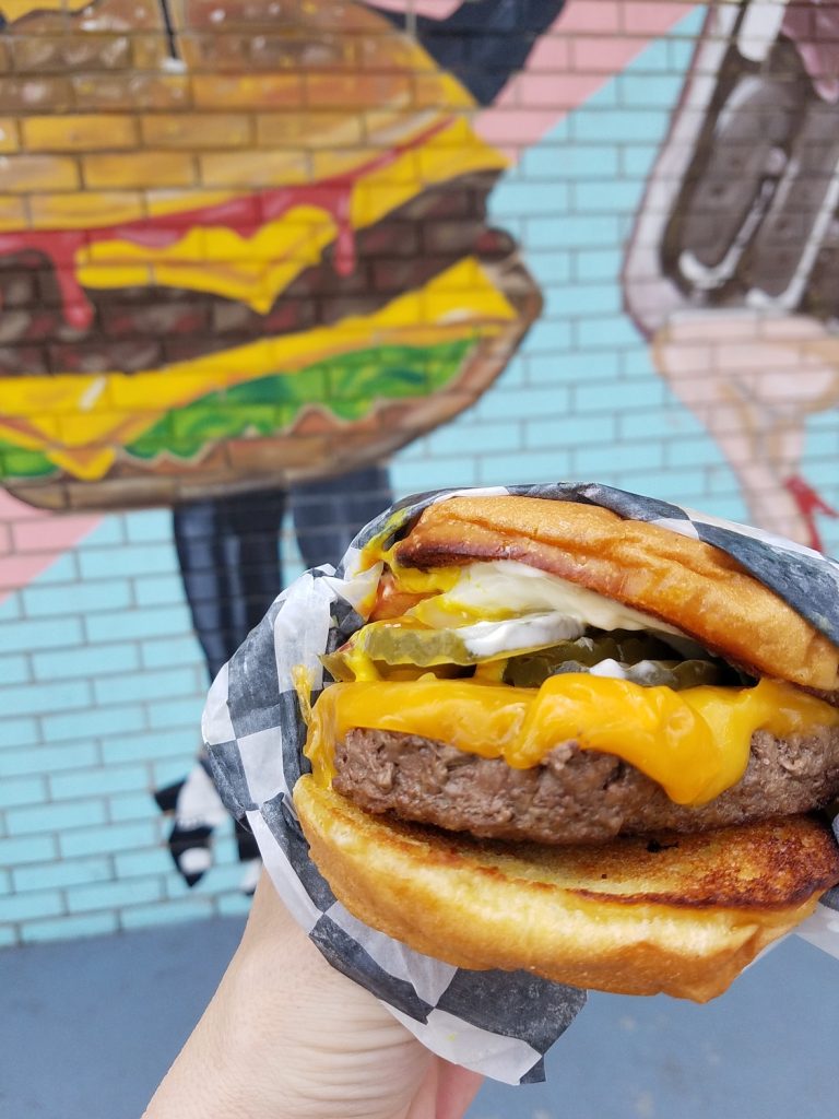 Cheeseburger being held in front of a mural featuring a painted cheese burger.