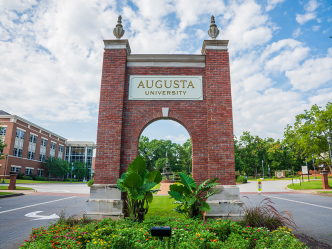 A brick archway with "Augusta University" carved into the front marks the entrance to a college campus.