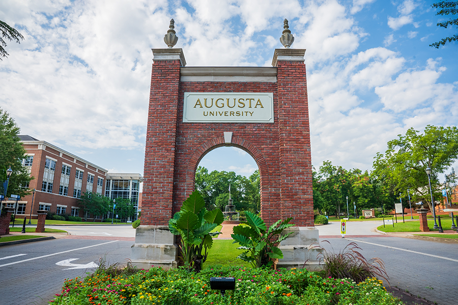 A brick archway with "Augusta University" carved into the front marks the entrance to a college campus.