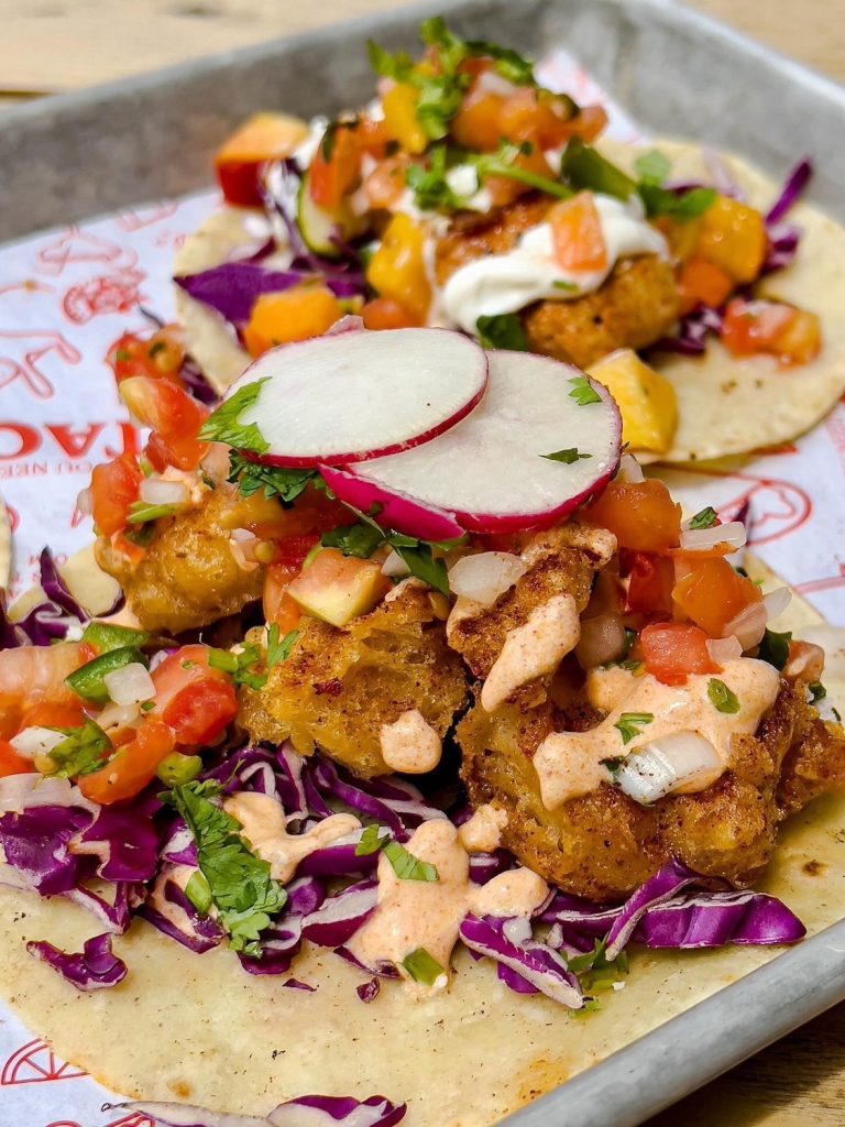 Soft tacos with chicken, pico de gallo, red cabbage, radishes and other toppings sit on a tray.