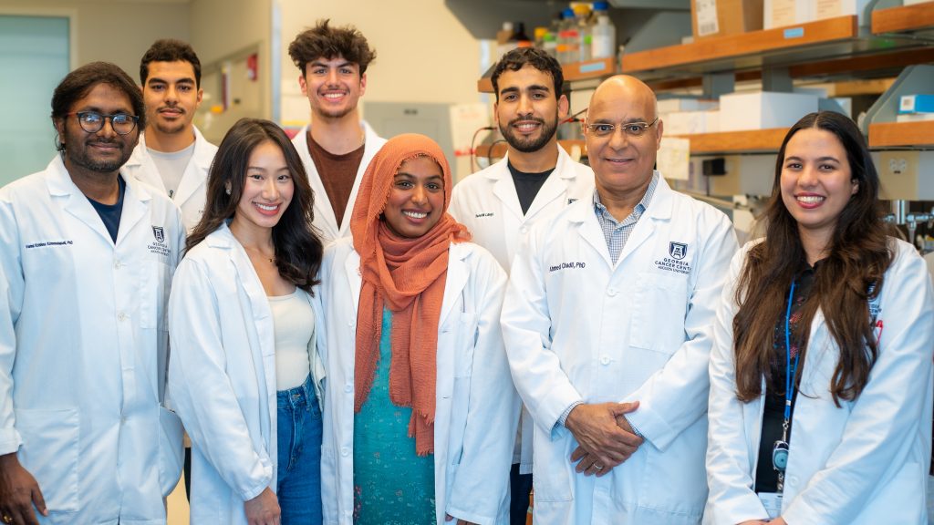 A group of scientists, all wearing lab coats, stand in a lab.