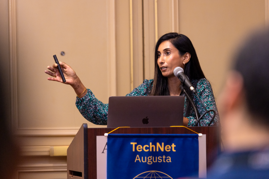 A female professor stands at a podium at the front of the room, presenting her research to conference attendees