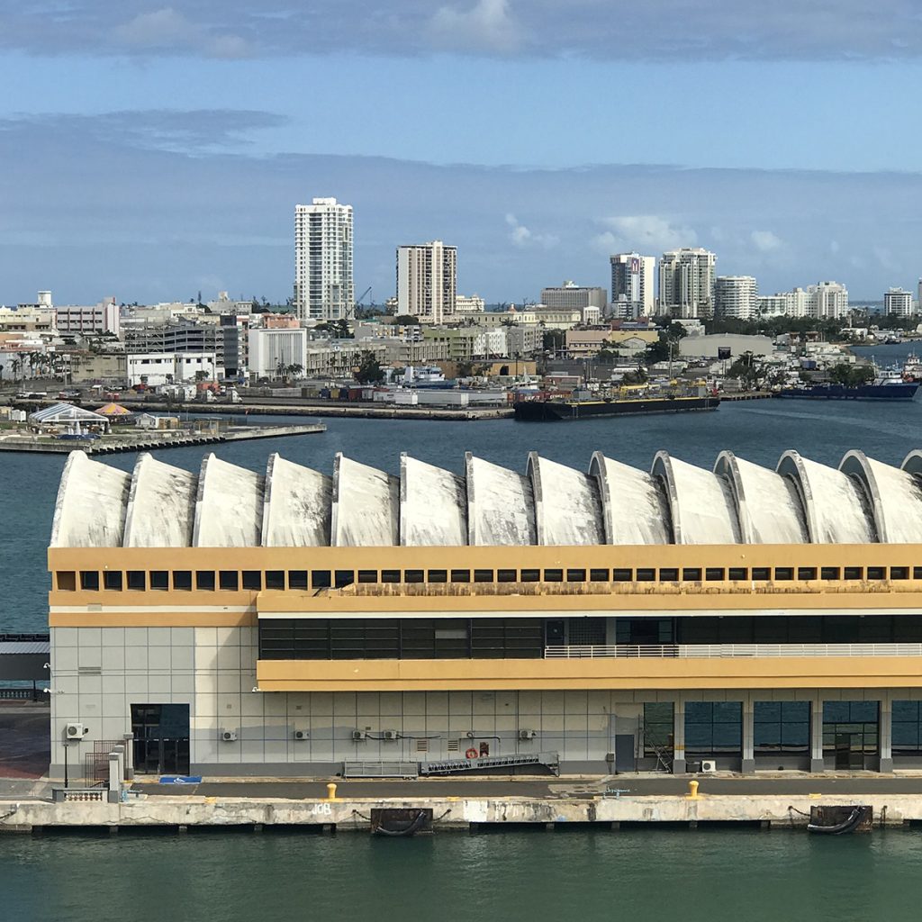 a town off the water is in the background while a big building with white half-spheres lining the roof sits in the water in the foreground