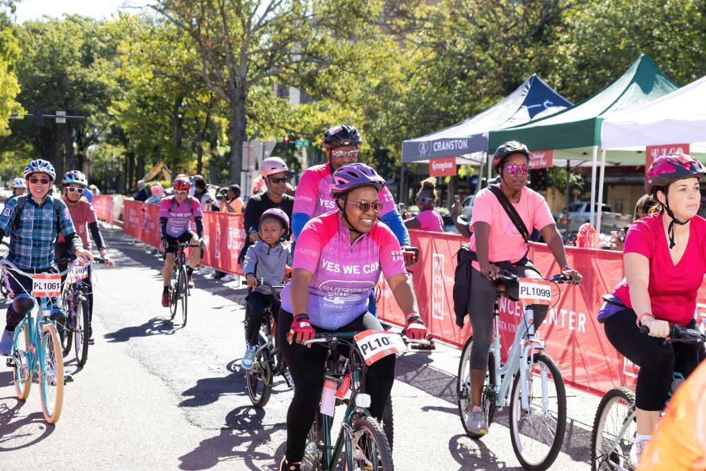 A group of riders with bike helmets and sunglasses smile as they come to the finish line.