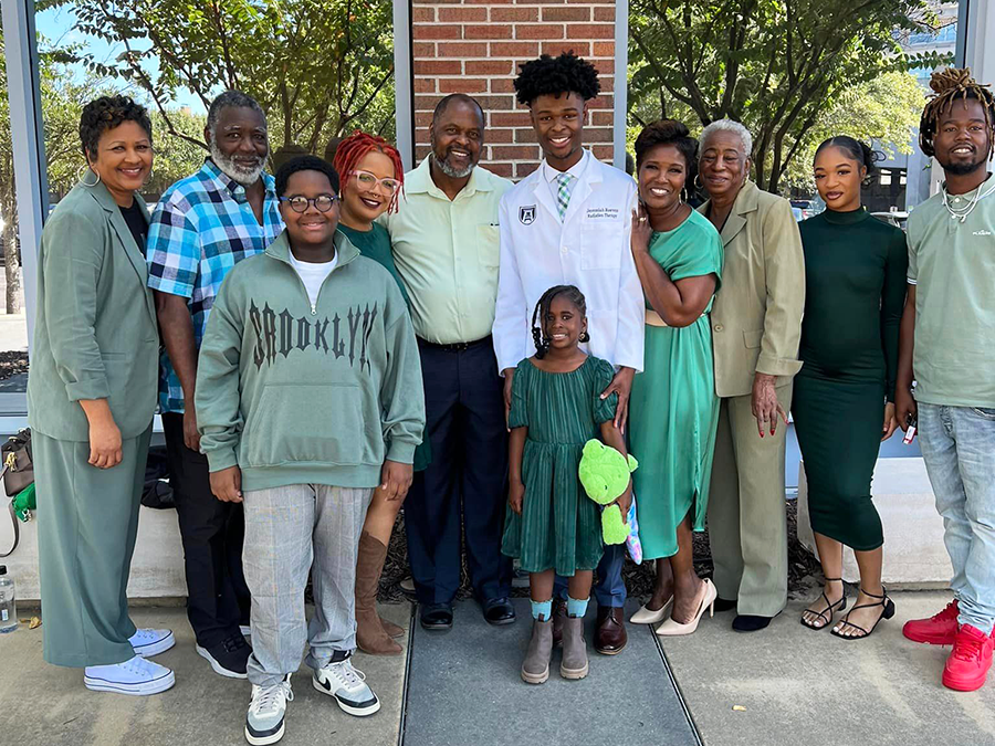 A man wearing a white medical professional's coat stands with his extended family outside.