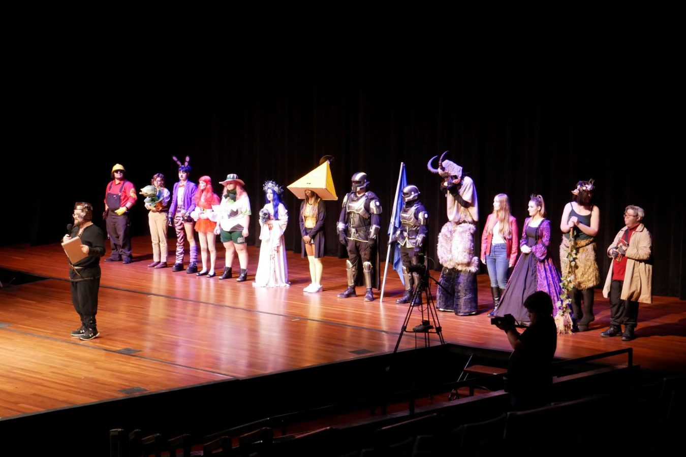 A large group of college students, all dressed in costumes from pop culture, stand on a stage during a costume contest.