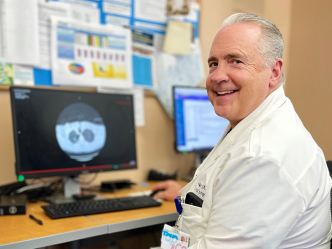 Man in a scientific lab coat sits at a computer with a microscope scan of a pair of lungs on the screen.