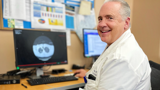 Man in a scientific lab coat sits at a computer with a microscope scan of a pair of lungs on the screen.