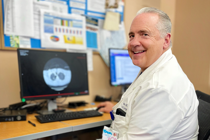 Man in a scientific lab coat sits at a computer with a microscope scan of a pair of lungs on the screen.