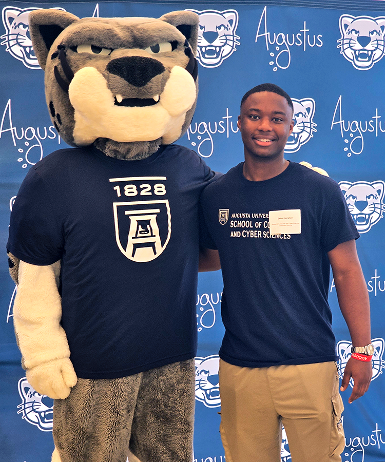 A male college student stands next to a college athletics mascot depicting a Jaguar.