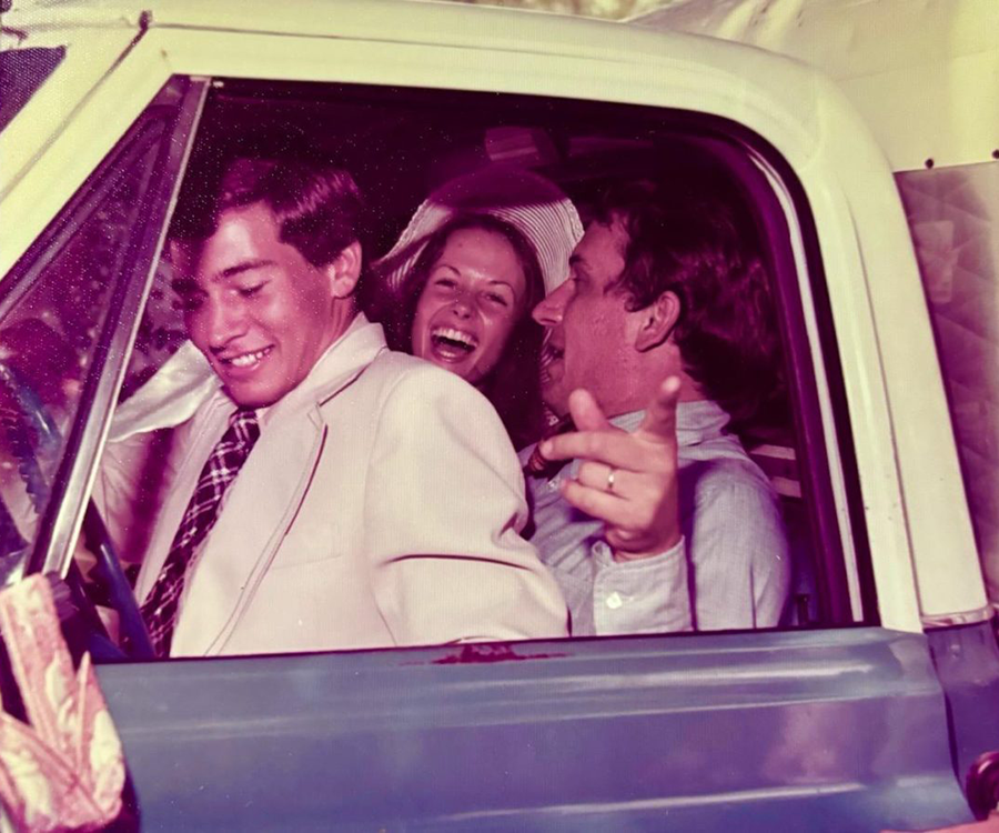 A vintage photo of three young adults laughing in the cab of a classic truck.