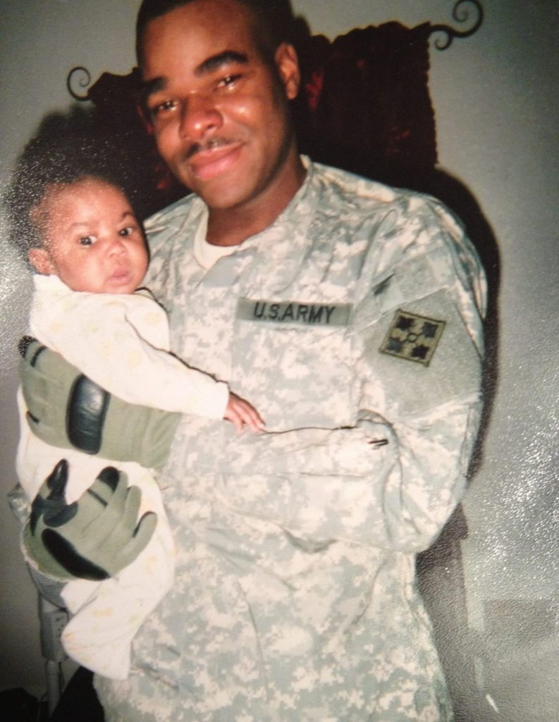 A man in an Army uniform is holding a baby.