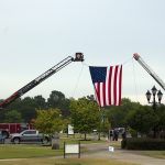 The American flag is raised by two cranes.