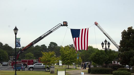 The American flag is raised by two cranes.