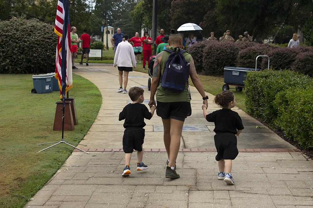 Woman holds the hands of two children while walking past an American flag on the side of the sidewalk.