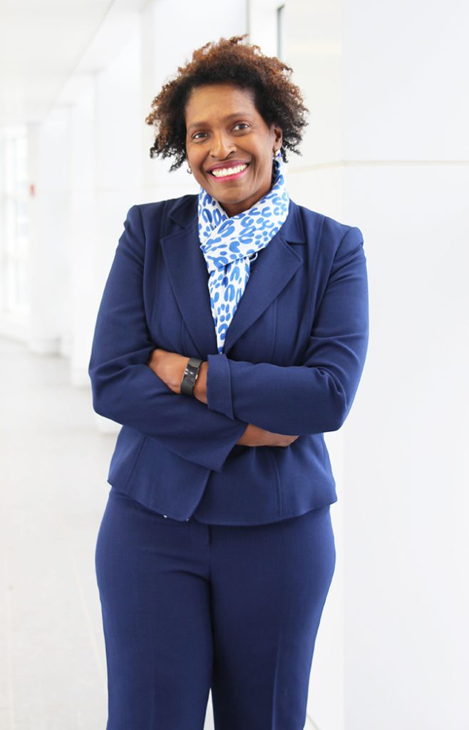 Woman in a navy suit poses with her arms crossed, smiling