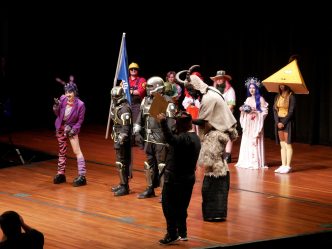 A large group of college students, all dressed in costumes from pop culture, stand on a stage during a costume contest.