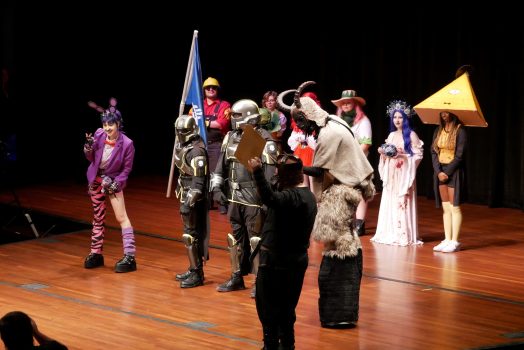 A large group of college students, all dressed in costumes from pop culture, stand on a stage during a costume contest.