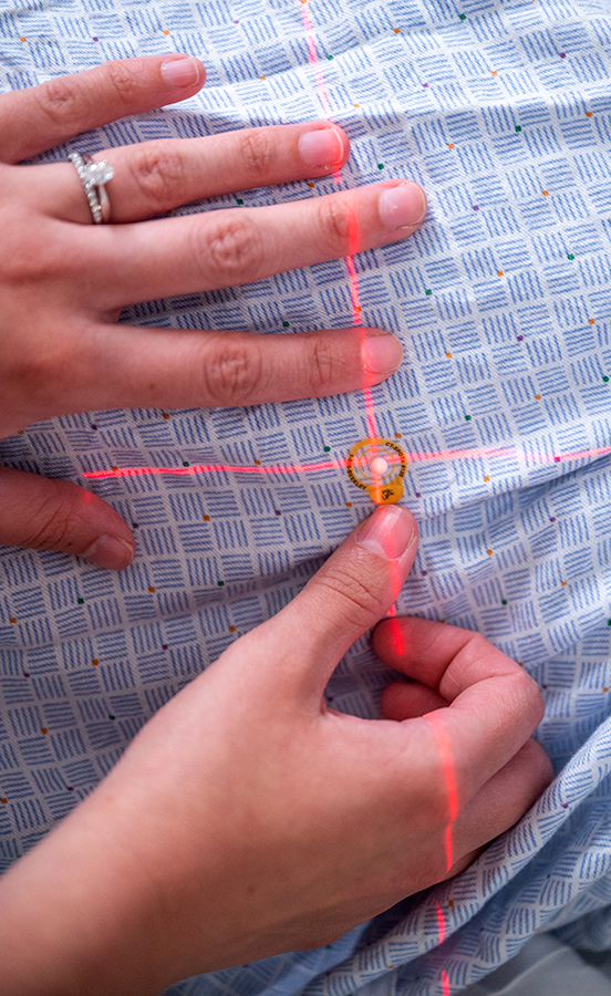 A woman places a small circular monitor on a patient wearing a medical robe.