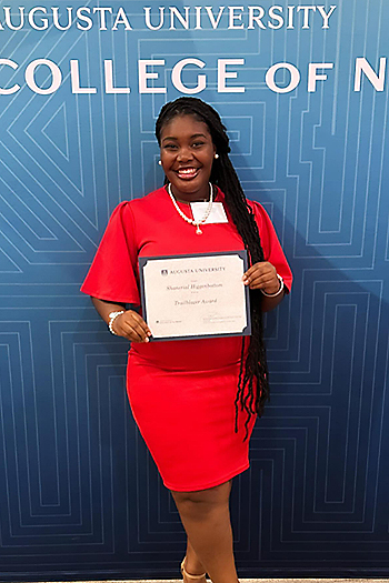 A woman in a red dress holds a certificate in front of an Augusta University College of Nursing backdrop.