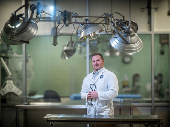 A man in a scientific lab coat stands in a lab.