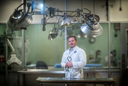 A man in a scientific lab coat stands in a lab.