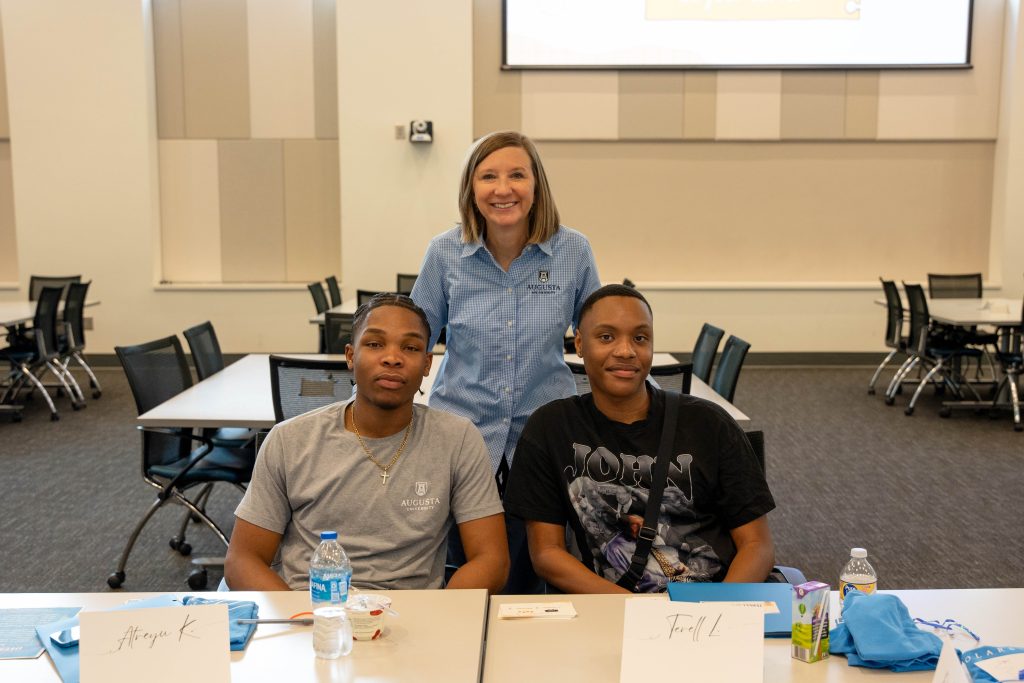 A woman stands behind two male students who are sitting at a table.