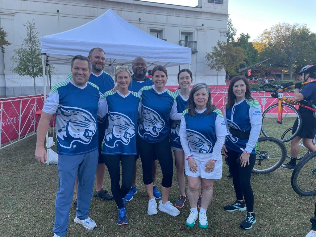 Eight people in matching bike shirts pose for a group photo outside.