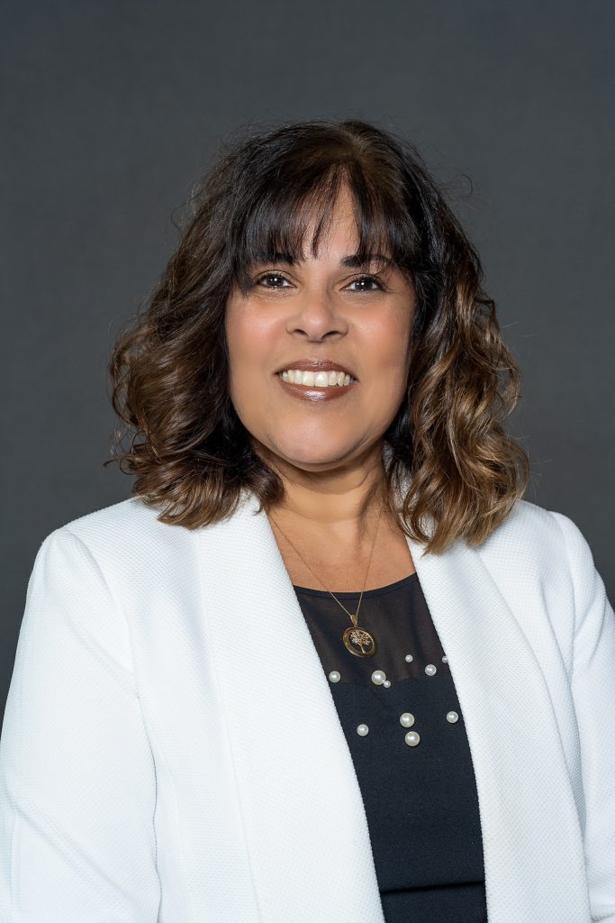 a woman wearing a white jacket and dark colored blouse smiles at the camera