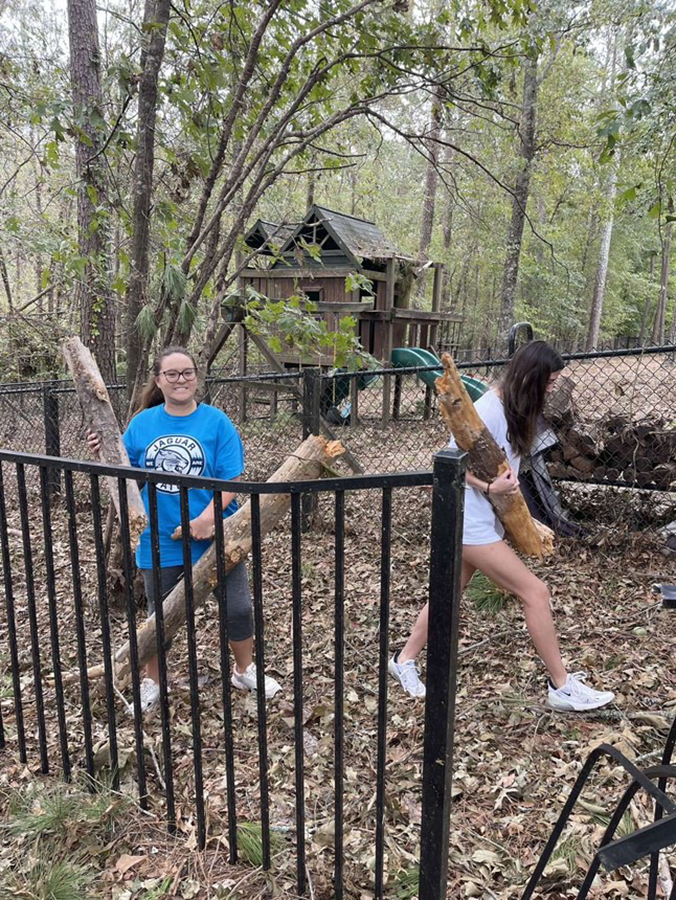 Two female college students work to clean up a yard following a natural disaster.