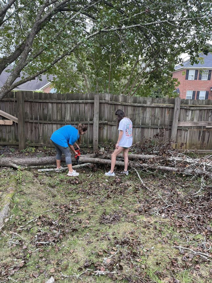 Two female college students work to clean up a yard following a natural disaster.