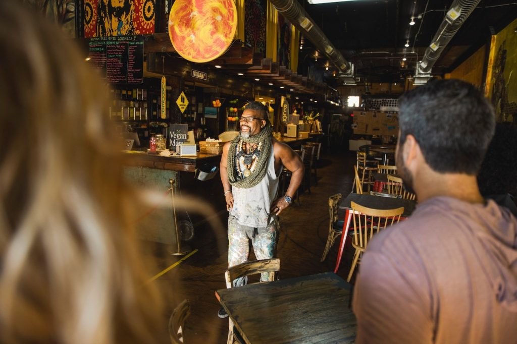 Man stands inside a restaurant talking to a tour group.