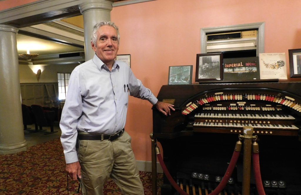 Man standing in theatre next to an organ.