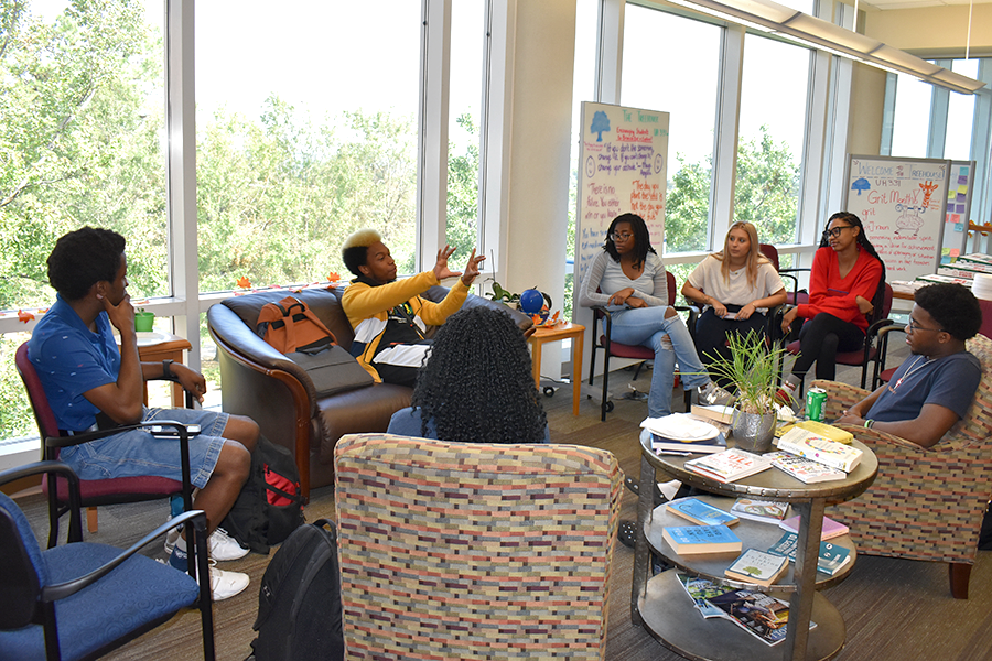 A group of eight college students sit in a circle in an office and talk about issues affecting them.