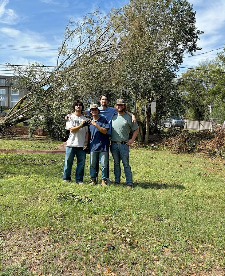 Four male college students work to clear a yard of debris following a natural disaster.