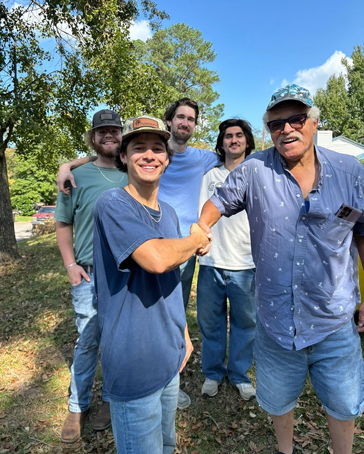 Four male college students speak with a homeowner after clearing his yard of debris following a natural disaster.