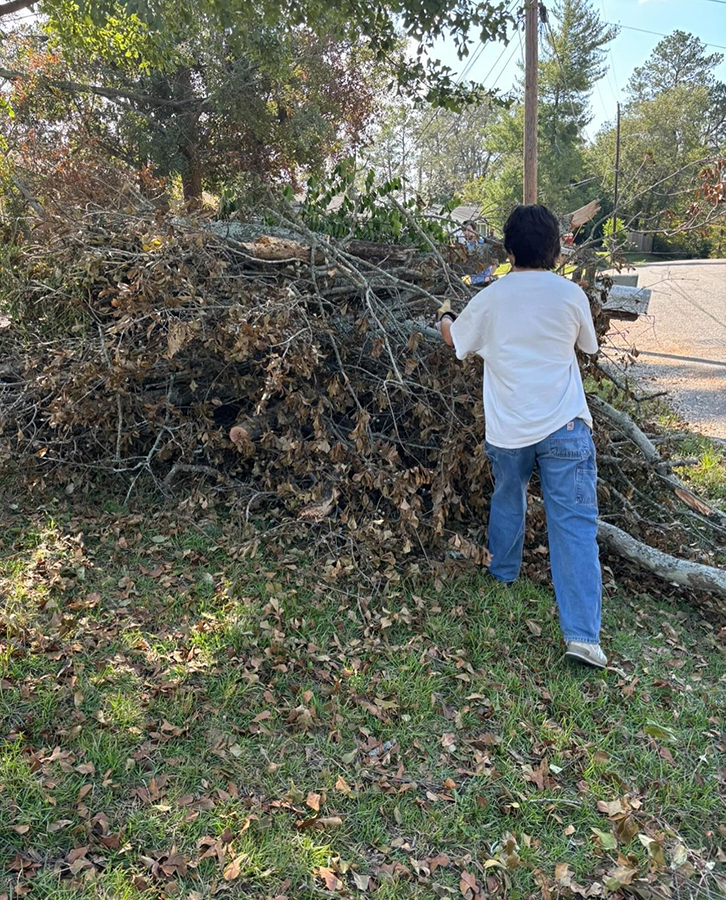 A male college student works to clear debris from a yard following a natural disaster.