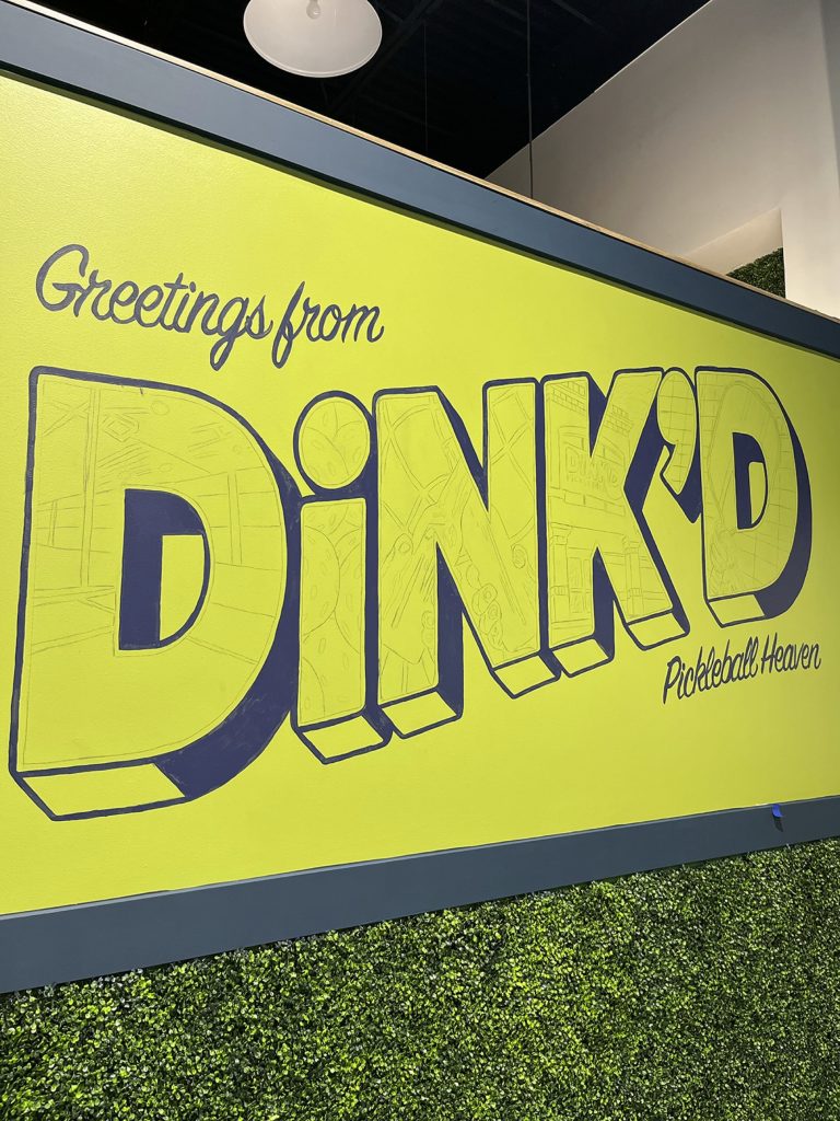 The first outlines of a mural in a pickleball facility with the words "Greetings from DiNK'D Pickleball Heaven."