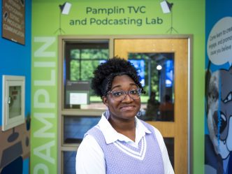 A woman stands in front of an entryway to a classroom with the words "Pamplin TVC and Podcasting Lab" above the door.