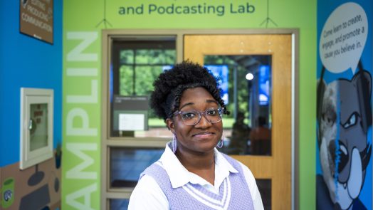 A woman stands in front of an entryway to a classroom with the words "Pamplin TVC and Podcasting Lab" above the door.