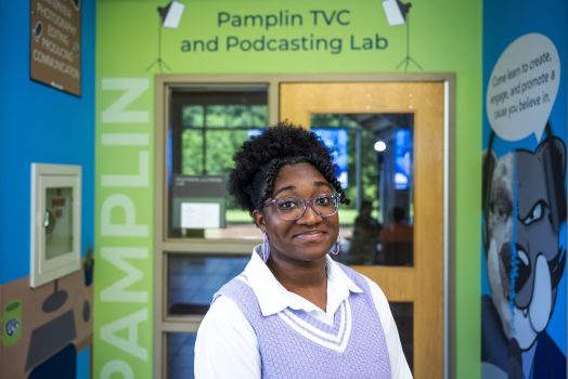 A woman stands in front of an entryway to a classroom with the words "Pamplin TVC and Podcasting Lab" above the door.