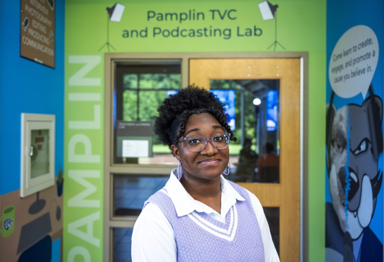 A woman stands in front of an entryway to a classroom with the words "Pamplin TVC and Podcasting Lab" above the door.