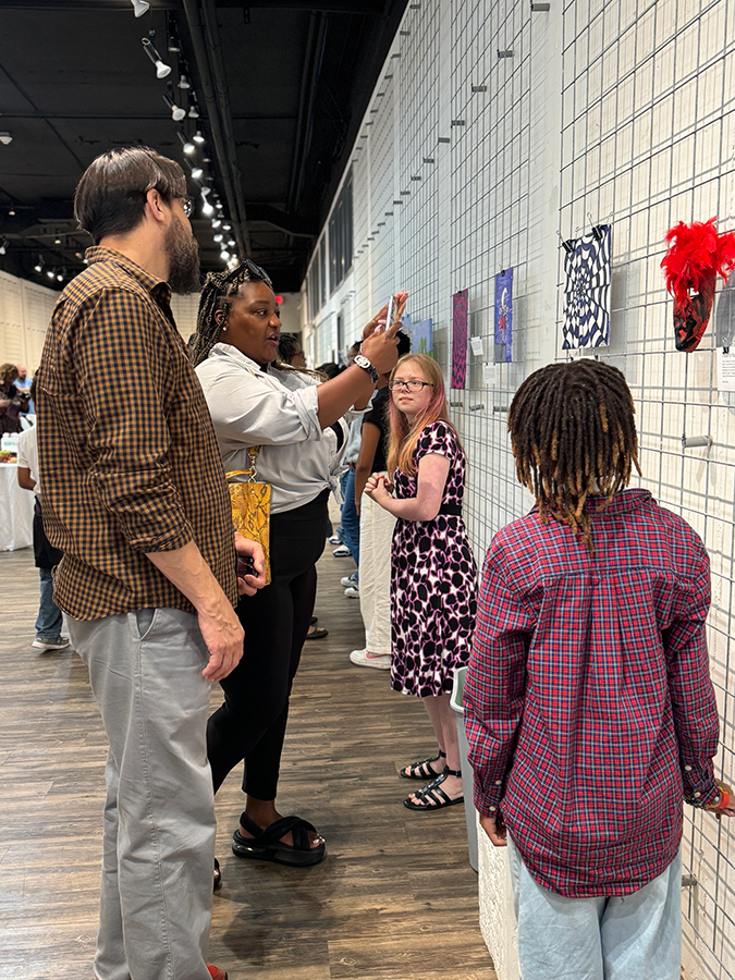 A man and a woman speak with young students during an art show.