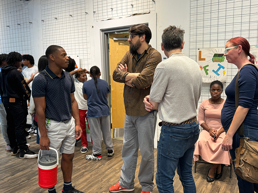 A man wearing glasses speaks with a young student during an art show.