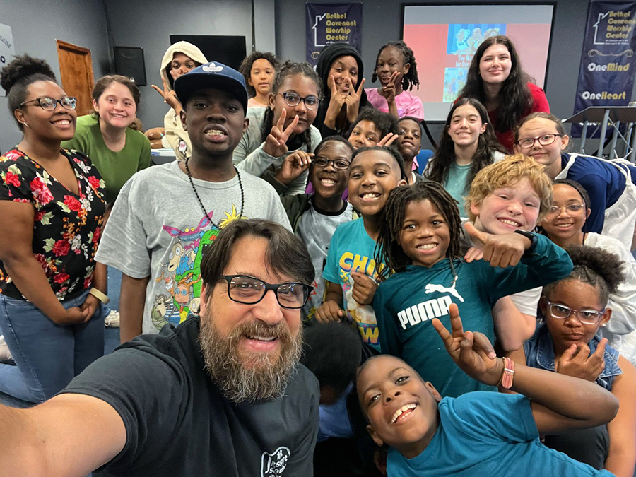 A man in glasses poses for a selfie with a large group of students.