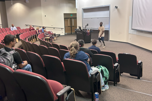 A group of people sitting in an auditorium facing a speaker.