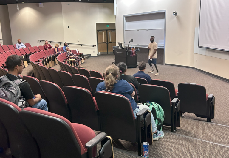 A group of people sitting in an auditorium facing a speaker.