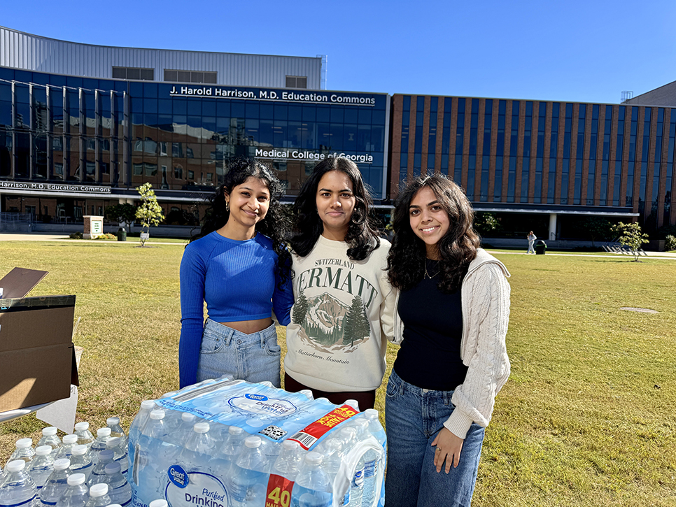 Three women smile while passing out non-perishable goods.